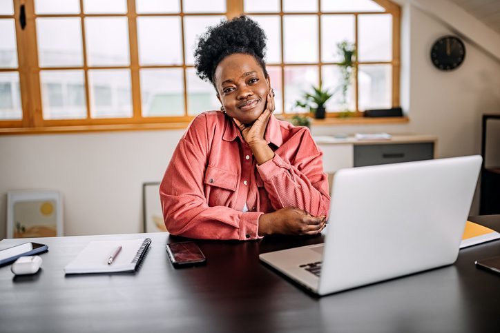 Confident black female business owner sitting at her computer smiling after completing an easy online loan application