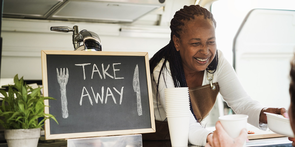 African woman serving takeaway food with eco paper boxes inside food truck