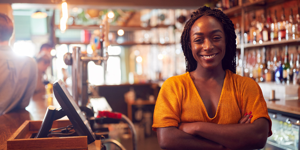 Portrait Of Smiling Female Bar Owner Standing Behind Counter