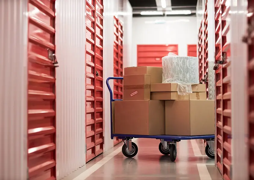 Blue cart with cardboard boxes in corridor of self-storage facility surrounded by locked red gates doors